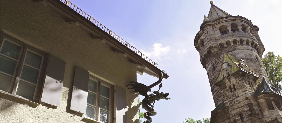 Blick nach oben, Drachenfigur unter dem Museumsdach, daneben Mutterturm in den Himmel ragend