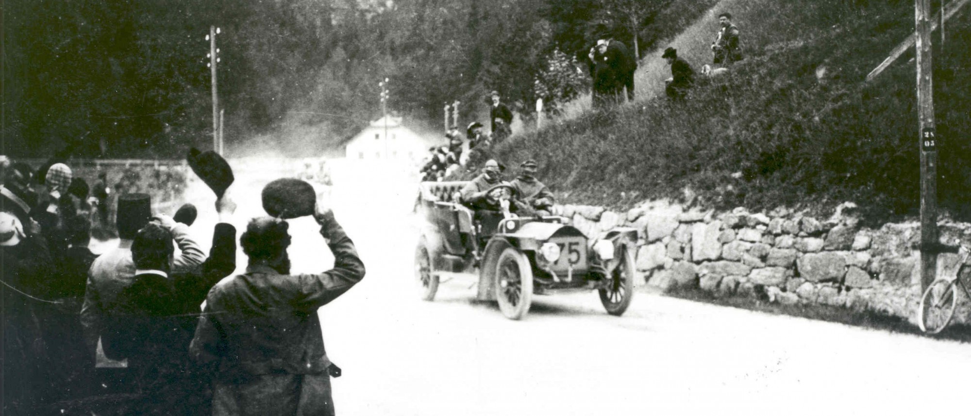 Schwarz-weiß-Foto Historisches Automobil fährt staubend an Zuschauermenge vorbei.